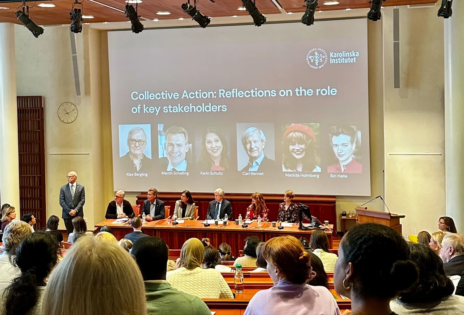 A panel of 6 persons sitting on the stage of an auditorium.