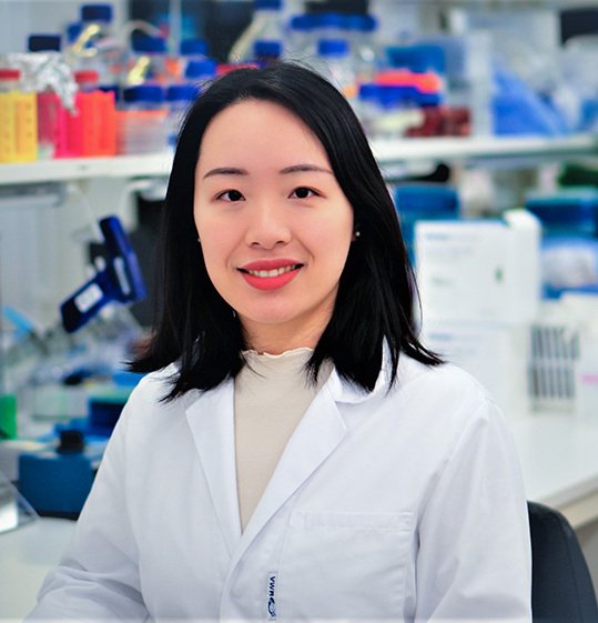 Young female researcher in a lab, wearing a white lab coat.