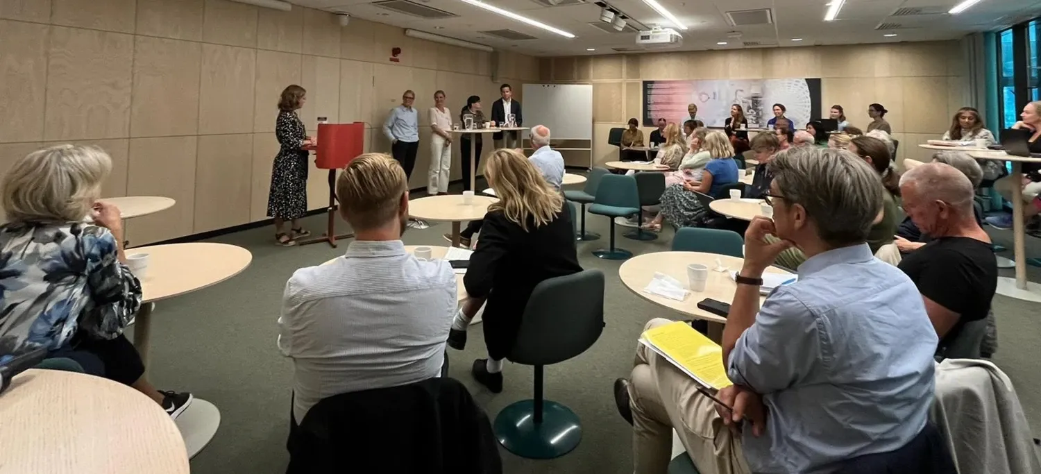 People sitting around tables in a room looking up front at a panel consisting of four people