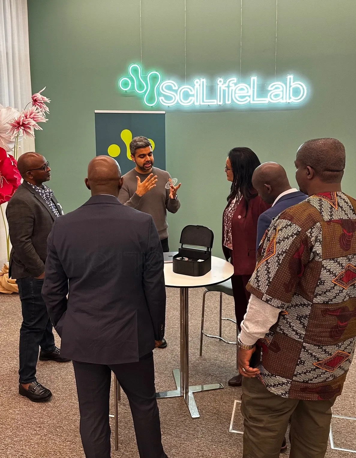 A man by a standing table showcasing a research device to five persons.