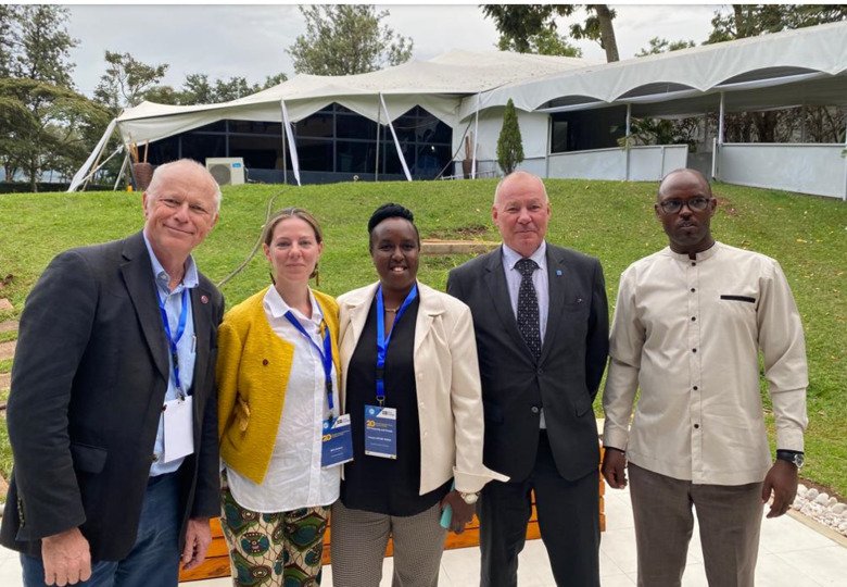 Group picture of the fice people standing in a row and in the background there is a a grassfield and white tents.