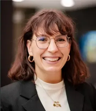 Close-up portrait of Simona Serra wearing a jacket, eyeglasses, and smiling at the camera