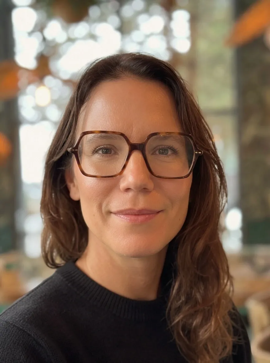 Portrait image of a dark haired woman with angular glasses and a black sweater.