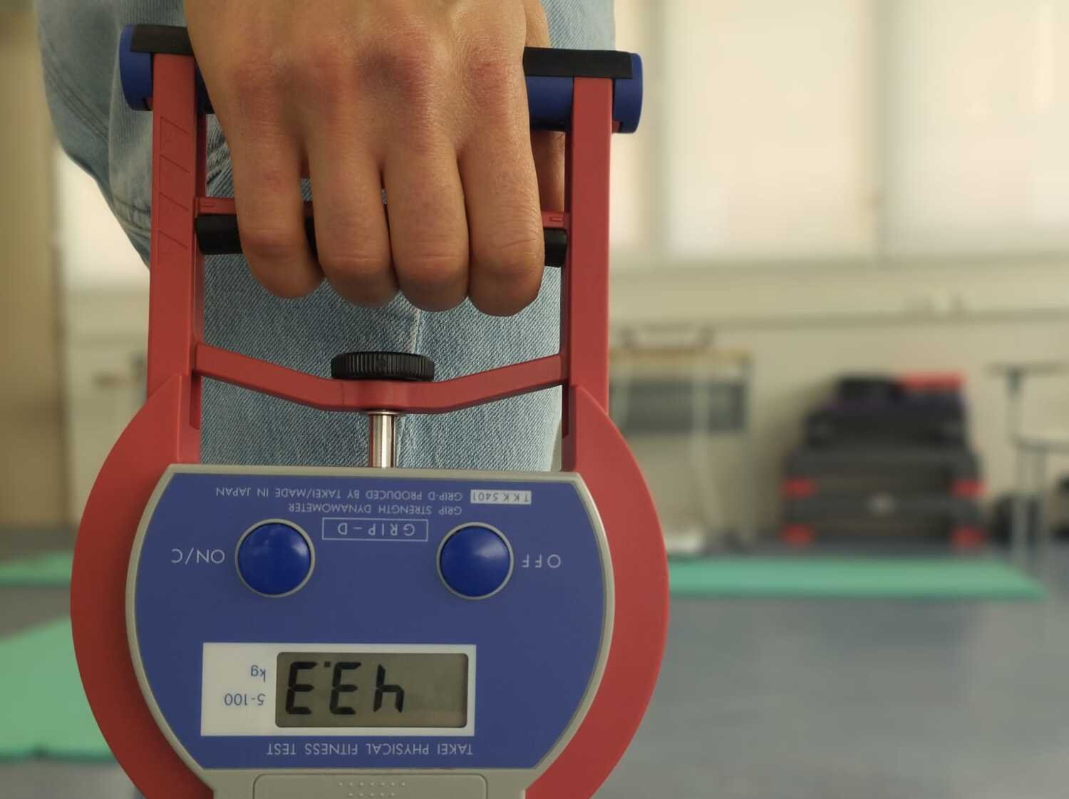 One hand holds a device that measures the hand’s grip strength.