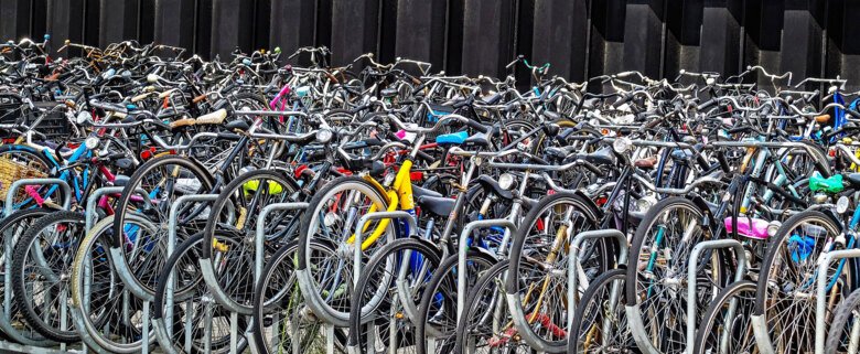 stor mängd cyklar som står vid cykelställ, utomhus