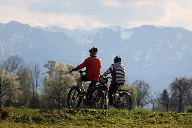 Two elderly people cycling in nature, they are both wearing helmets.