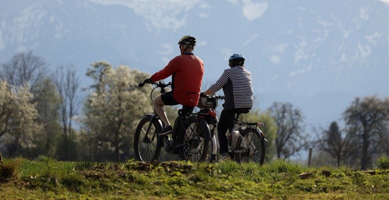 Two elderly people cycling in nature, they are both wearing helmets.