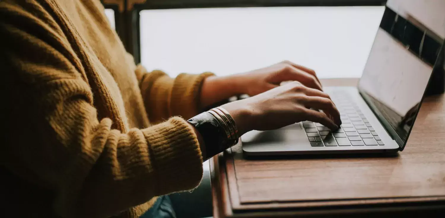 Close-up of a woman in a yellow shirt, sitting in front of a computer, typing