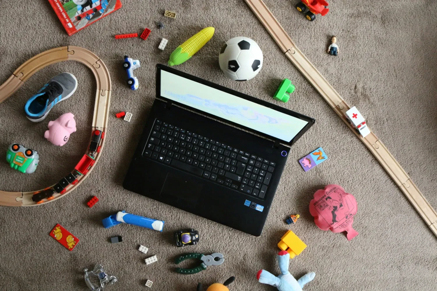 An open laptop on a floor where lots of children's toys are scattered.