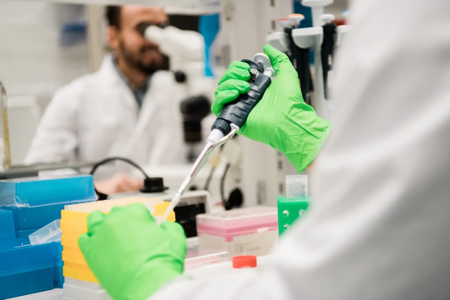 A person pipetting with green gloves on.