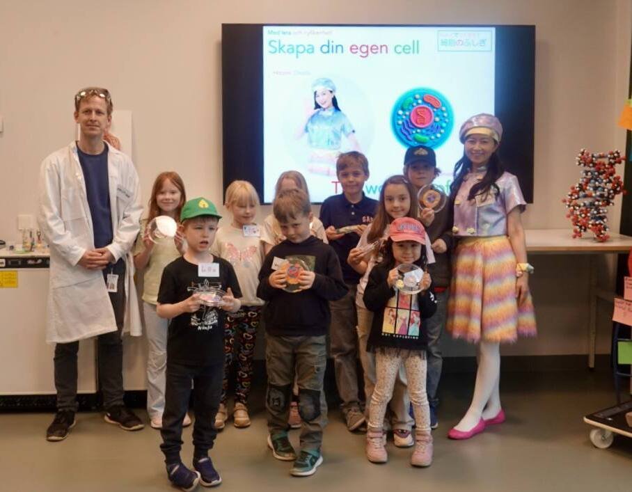 A group of children pose with their clay cells together with a researcher and Japanese artist Hitomi Okada.