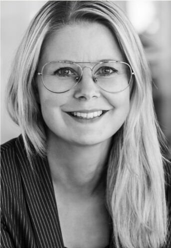 Black and white portrait of smiling woman, with long blonde hair and glasses.