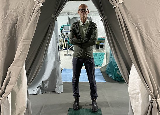 A mans standing in the entrance to a tent. The tent is a field hospital