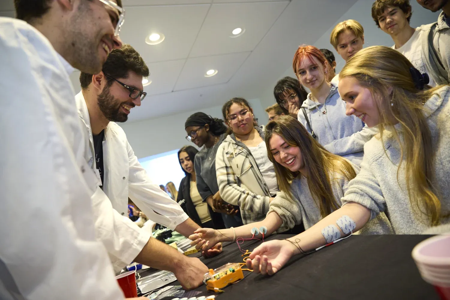 High school girls sitting at a table with cords on their arms.