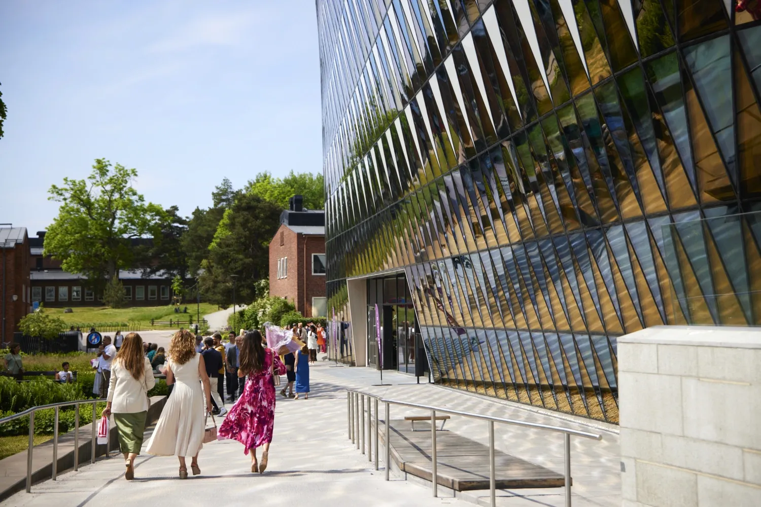 Colorfully dressed students walk next to the Aula Medica under a clear blue sky.