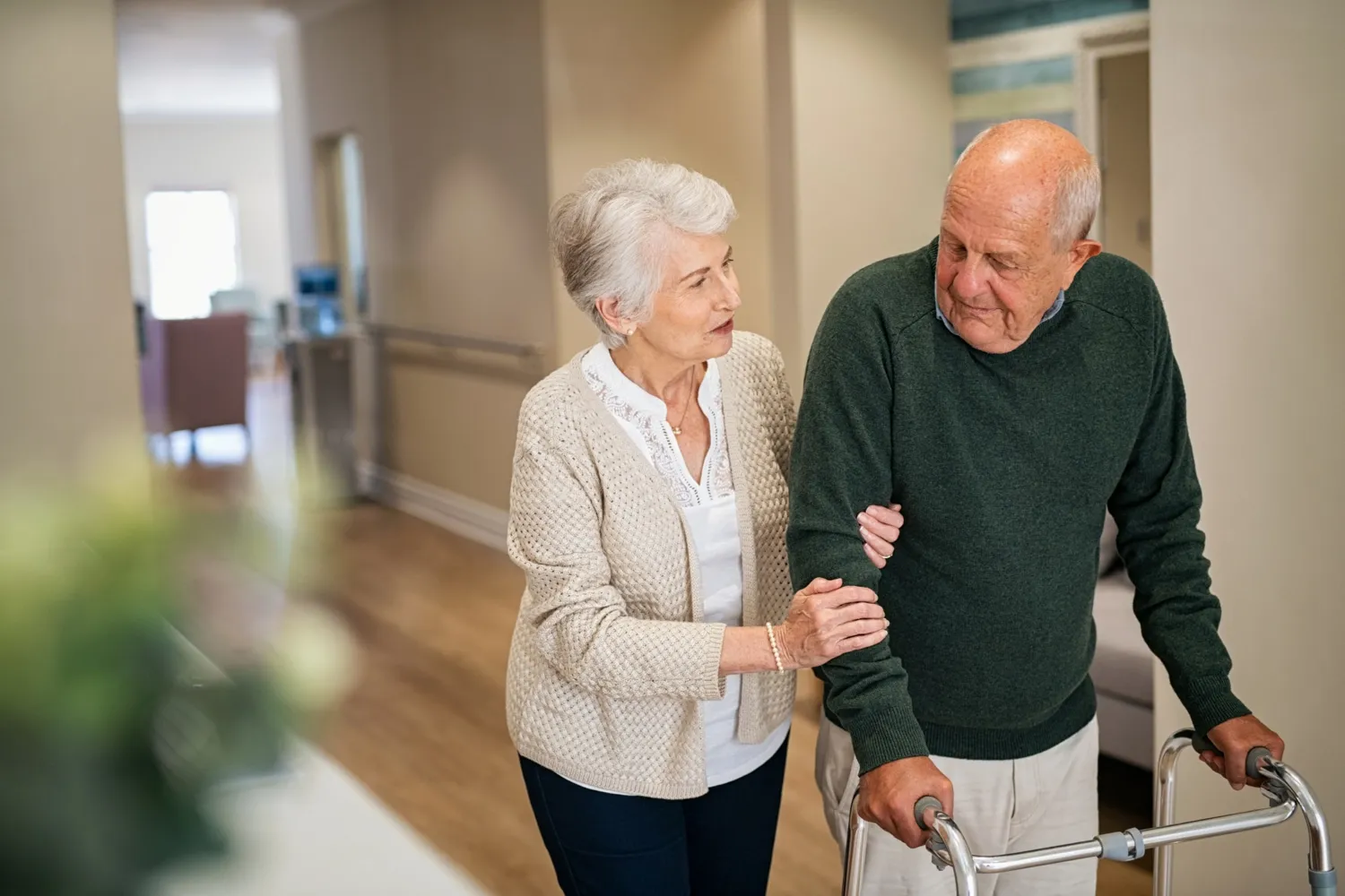 Elderly woman helps an elderly man to walk with the aid of a walker.