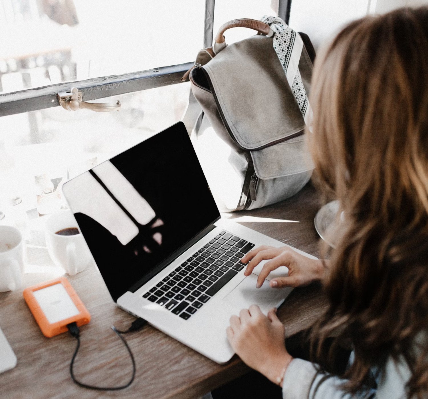 A woman sits with her back to the camera in front of a laptop.