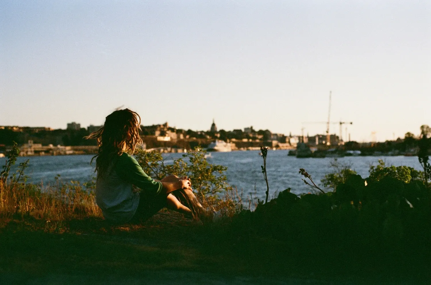 Young person sitting on a mountain ridge in Stockholm, looking out over the water and the city.