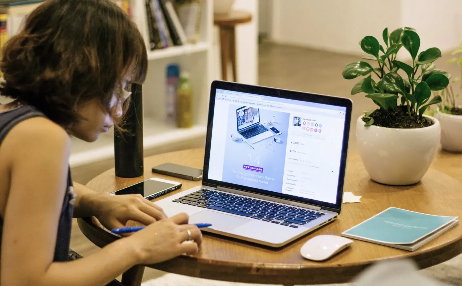 Photo of an Asian woman taking notes on a writing pad next to an open laptop