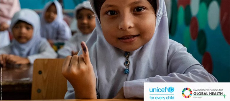 Young girl in headscarf holds up littlefinger that has some black paint on it.