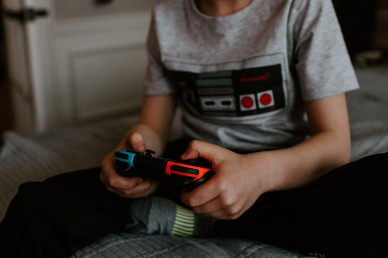 Boy holding video game controller, sitting on bed.