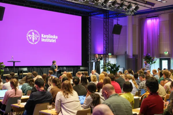 People attending a conference, with a speaker on stage