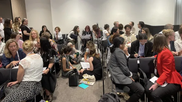 A lecture hall packed with conference participants, seated both at desks and on the floor.