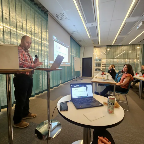 Photo of Mark Issa standing with a microphone in front of an audience in a larger meeting room