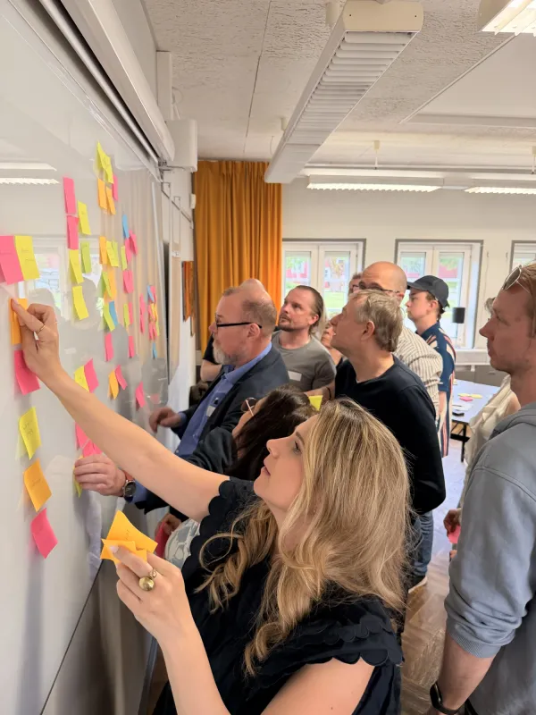 Photo of people working together and sticking Post-it notes on a whiteboard.