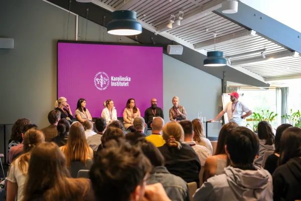 People attending a discussion, with 6 panelists on stage