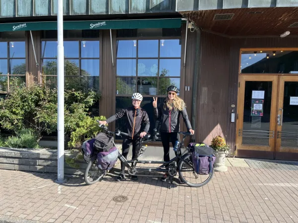 Pernilla and Oskar are standing in front of the hotel with their tandem bicycle in front of them.