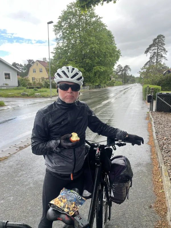 Oskar Jonsson is having an apple standing by the tandem bike, alongside the road.
