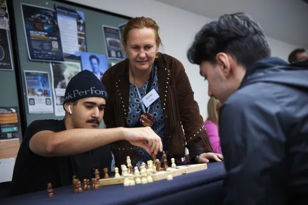 Two guys play chess, a woman (researcher) watches.