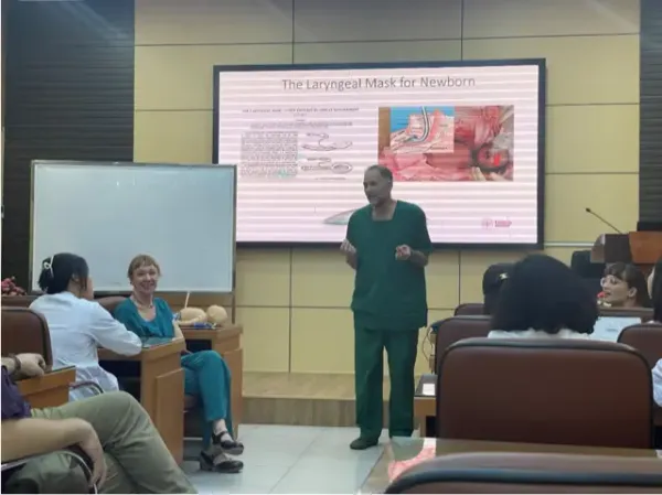 Susanna Myrnets Höök and Nicolas Pejovic presenting upcoming studies to the Neonatal Department at Phu San Hospital in front of projector screen wearing green hospital clothes.