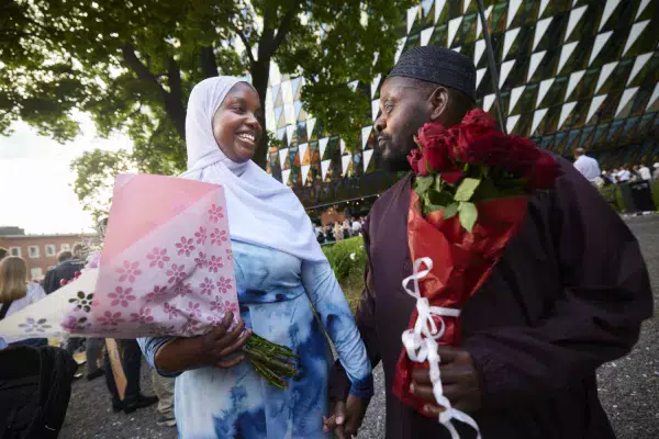 A graduation student is holding a flower bouquet and looking happily at her father.