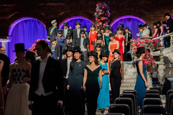 New doctors with their doctoral hats are walking down the stairs in the Blue Hall.