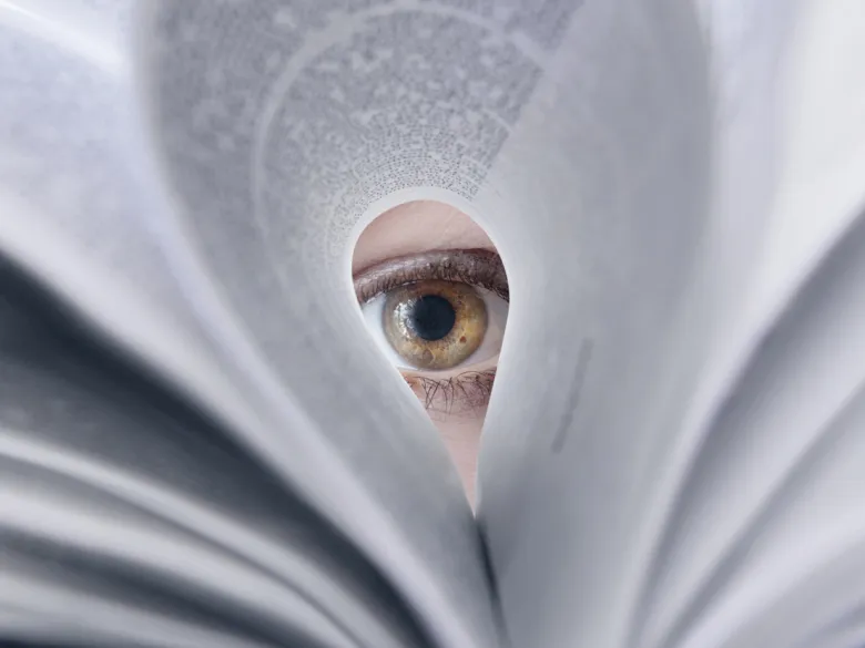 An eye looking through a folded book page.