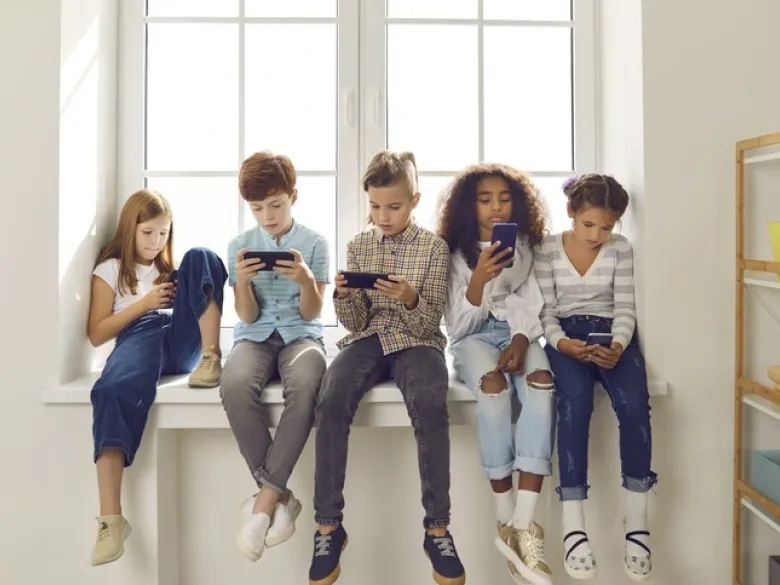 Children sitting next to each other, watching their phones.