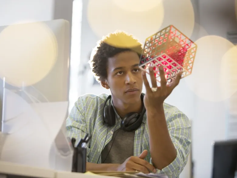A young man in deep thought. He is looking at a cube that he is holding in his hand.