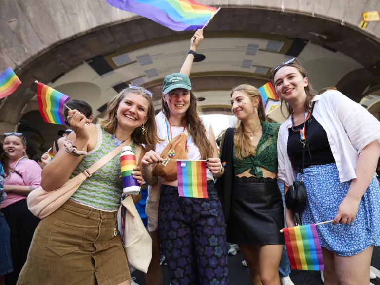 Alina Lapp, Maureen Verdier, Teresa Reindl and Katharina Schormair smiling in the street at the parade holding rainbow flags.