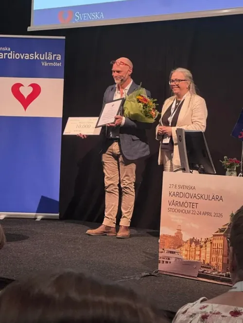 Andreas on a stage with a fram prize and flowers.