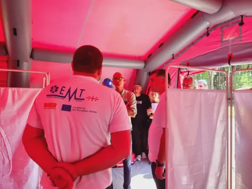 People standing in a hospital tent. The man closes to the camera as a t-shirt with the text WHO EMT on the back