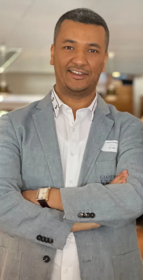 Portrait of a man, wearing a grey jacket, standing with his arms crossed.