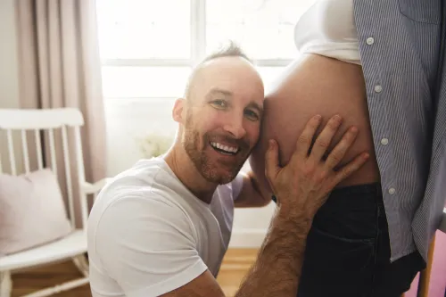A man with his face at a pregnant belly
