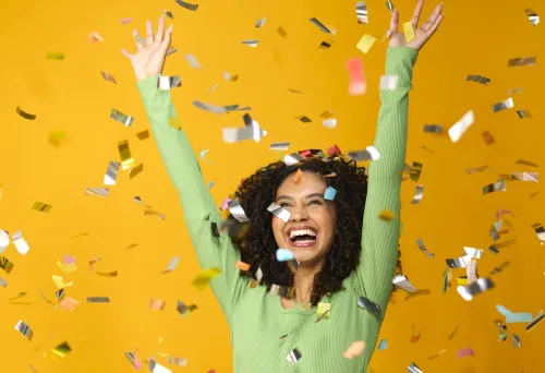 Happy girl with arms in the air surrounded by confetti.