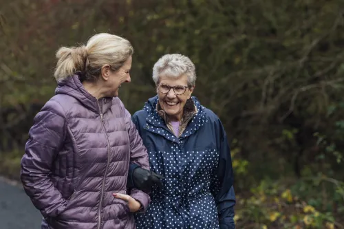 Stock photo showing a woman in her late middle age walking with an older woman.