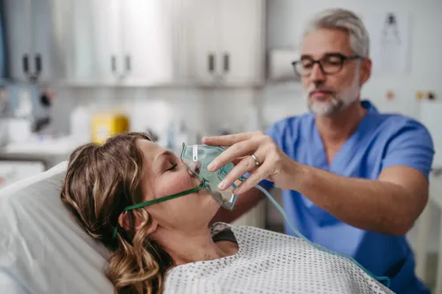 Doctor putting oxygen mask on patient face. Male nurse taking care of unconscious patient in intensive care unit.