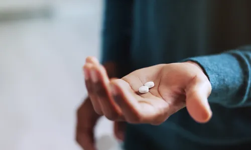 Decorative image with a person holding pills for medication in their hand.