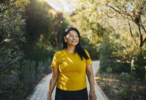 Image of a smiling woman in a yellow short-sleeved shirt who is out for a walk in sunny and clear weather.