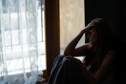 Depressed woman sitting by the window in her bedroom